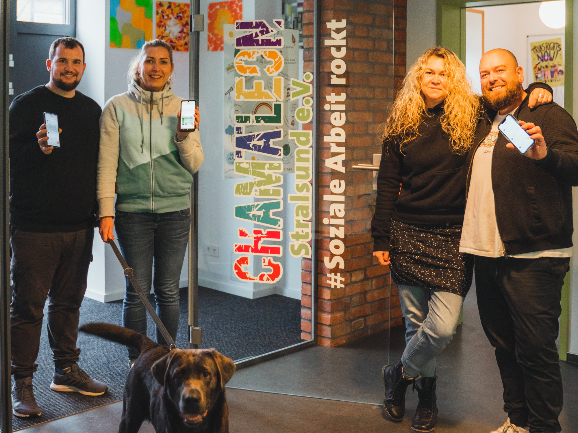 Vier Mitarbeiter des Chamäleon Stralsund e.V. stehen vor dem Eingang der Einrichtung. Auch ein Labrador schaut neugierig in die Kamera. 