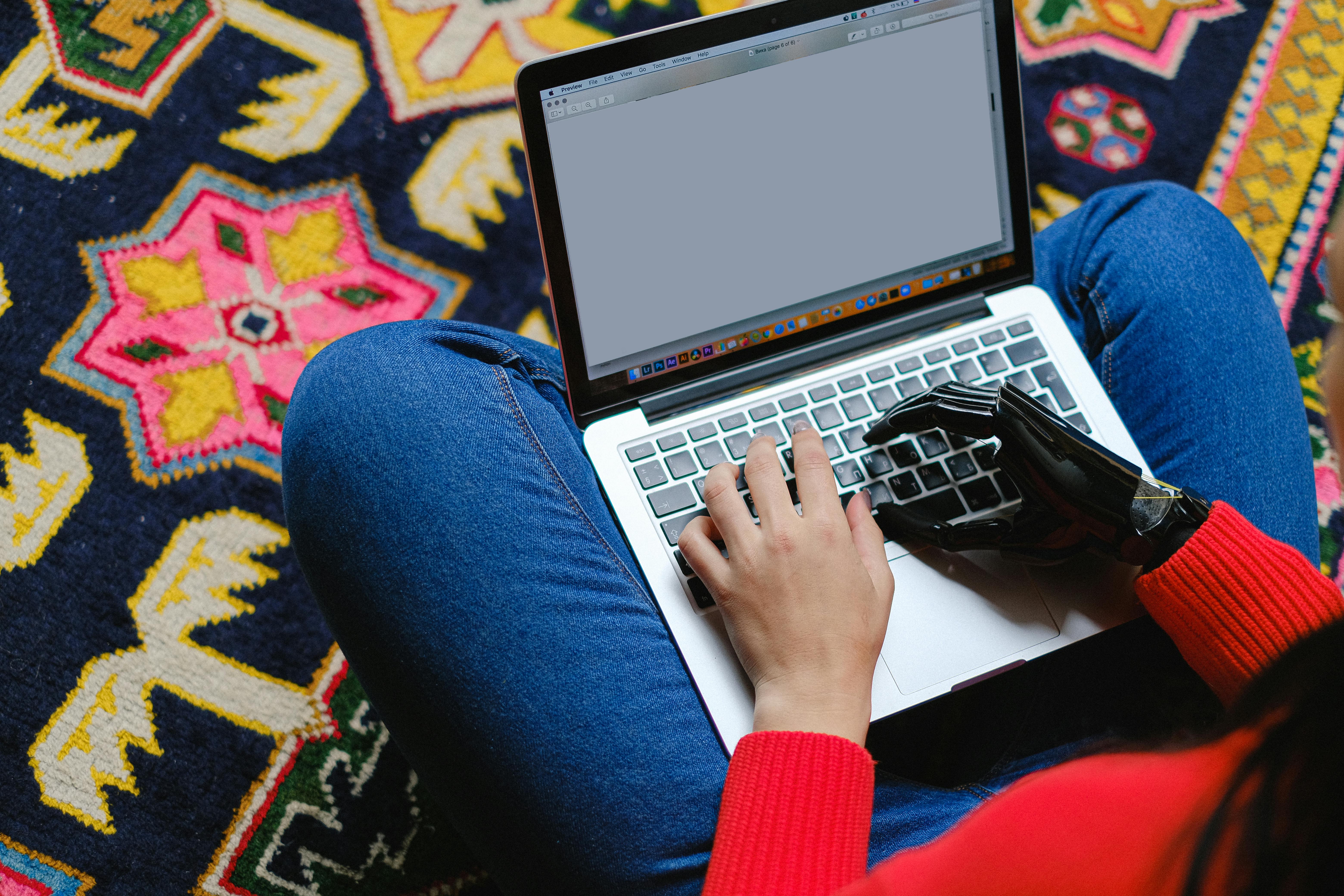 Eine Frau sitzt im Schneidersitz mit einem Laptop auf den Beinen. Ihre linke Hand ist eine bionische Version.